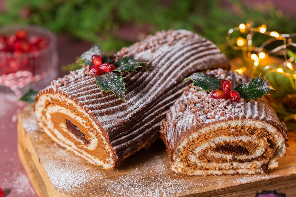 immagine di un tronchetto di natale, dolce tradizionale composto da un rotolo di pan di spagna farcito con crema al cioccolato e rivestito da glassa al cioccolato e granella per simulare la corteccia dell'albero.