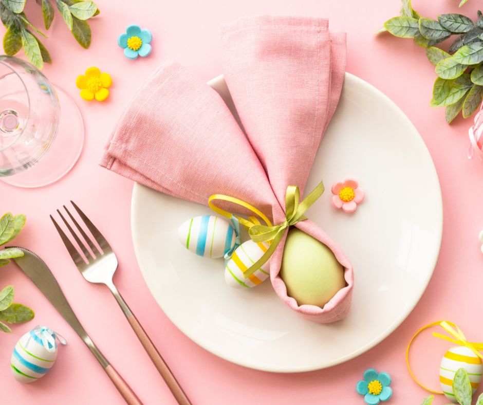 esempio di segnaposto decorativo per la tavola del pranzo di pasqua con un tovagliolo avvolto intorno ad un uovo colorato per creare l'effetto orecchie da coniglio, con aggiunta di fiori decorativi e ovetti di cioccolato per rendere la tavola festosa per la giornata